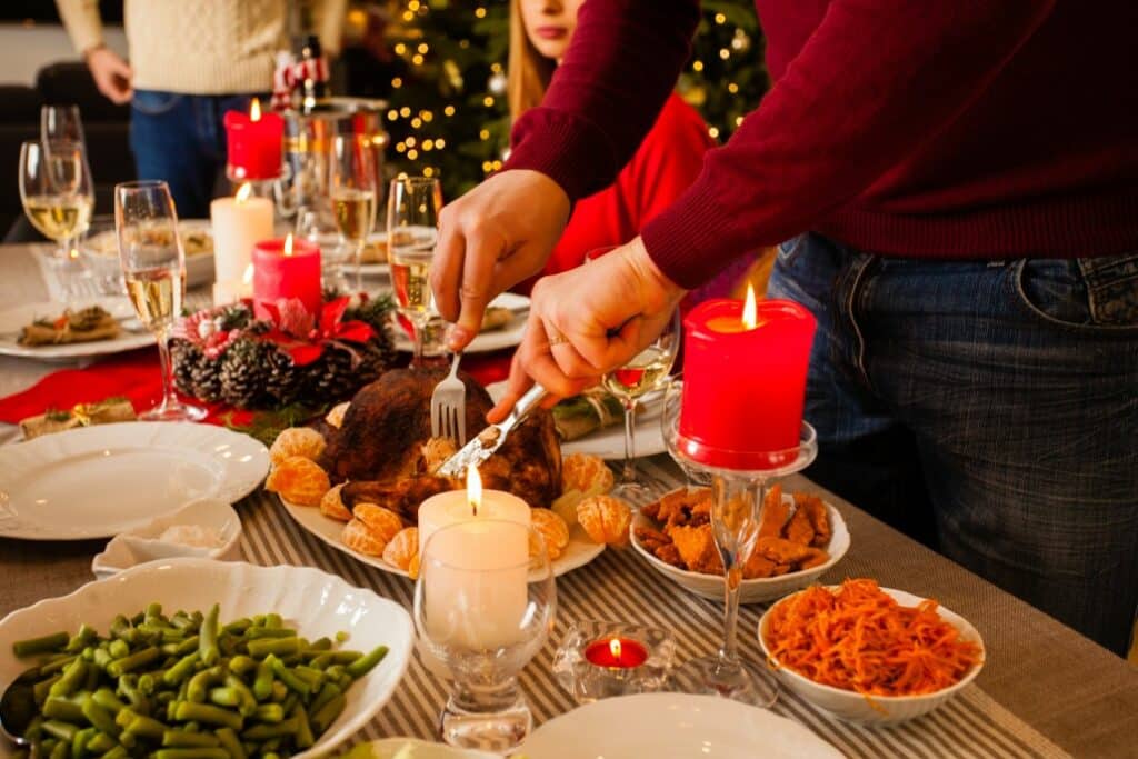 close up view of roasted turkey cut by mans hands table with christmas decor full of delicious food t20 OJezpL 1